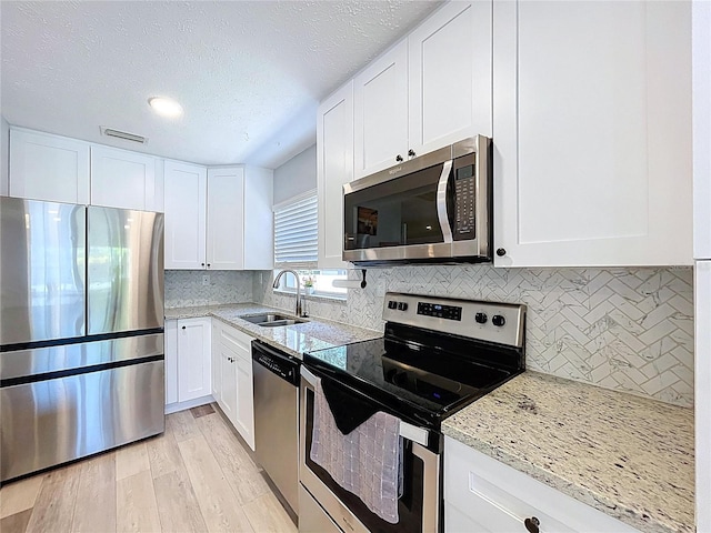 6811 S Himes Ave, Tampa, FL 33611 - kitchen with stainless steel appliances, a sink, light wood-type flooring, white cabinetry, and light stone counters