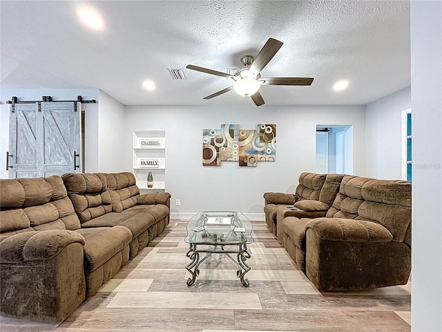 6811 S Himes Ave, Tampa, FL 33611 - living room featuring a ceiling fan, light wood-style flooring, a barn door, a textured ceiling, and recessed lighting