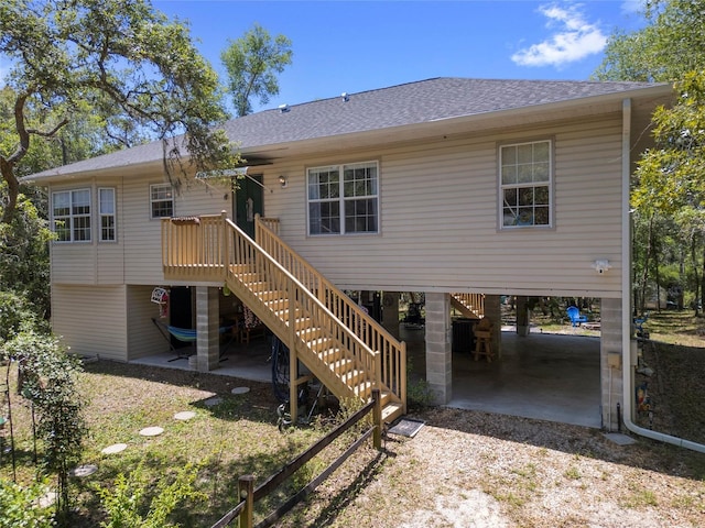 back of house featuring a carport, driveway, roof with shingles, and stairs