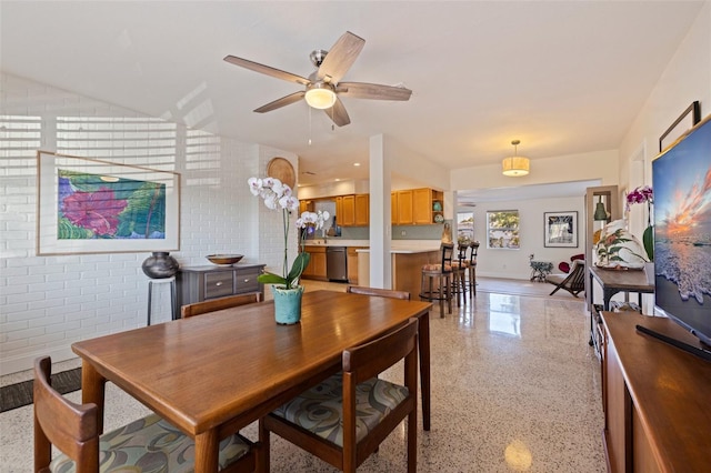 dining area featuring ceiling fan, light speckled floor, and brick wall