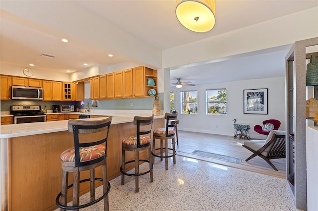 kitchen with a ceiling fan, glass insert cabinets, light countertops, backsplash, and appliances with stainless steel finishes