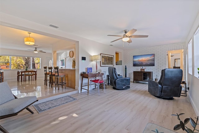 living area featuring wood finished floors, ceiling fan, a fireplace, baseboards, and visible vents