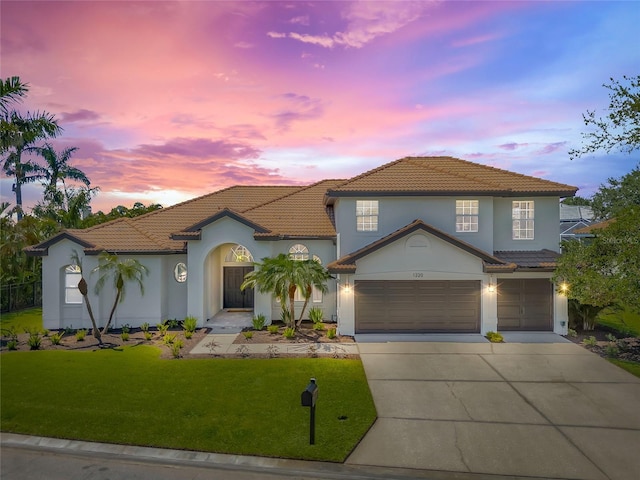 view of front of home featuring a tiled roof, driveway, a yard, and stucco siding