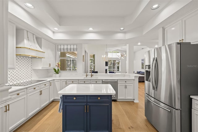 kitchen featuring light countertops, blue cabinets, a peninsula, appliances with stainless steel finishes, and custom range hood