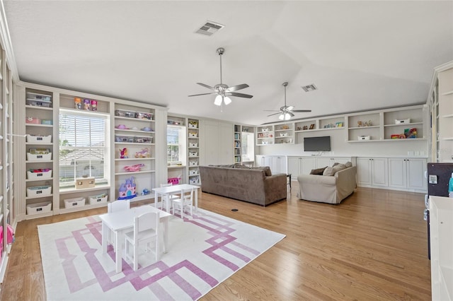 living area featuring vaulted ceiling, visible vents, a ceiling fan, light wood-style floors, and built in shelves