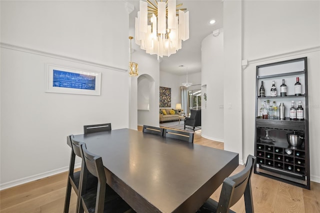 dining space featuring wood finished floors, a chandelier, arched walkways, baseboards, and recessed lighting