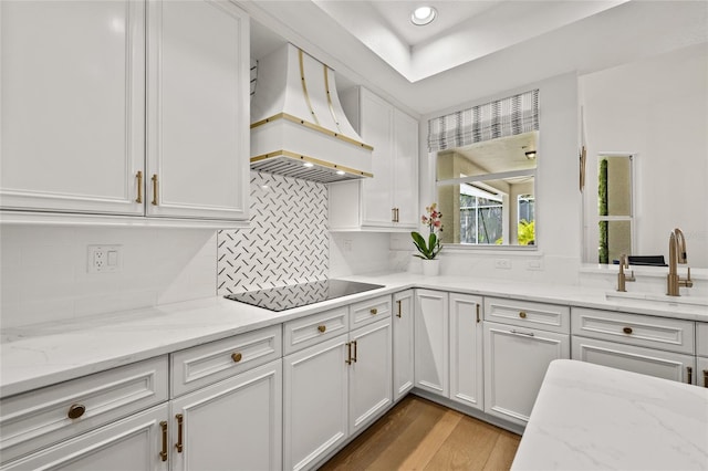 kitchen with white cabinets, a sink, light wood-type flooring, black electric stovetop, and custom exhaust hood