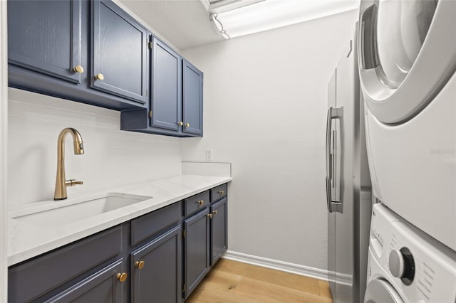 laundry area featuring a sink, light wood-type flooring, cabinet space, stacked washer / drying machine, and baseboards