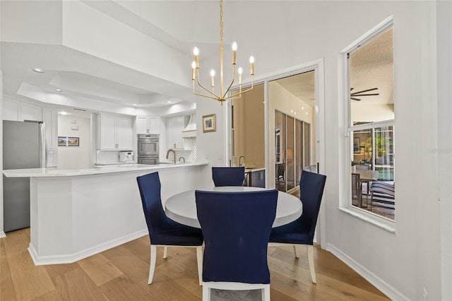 dining area featuring recessed lighting, light wood finished floors, a tray ceiling, baseboards, and ceiling fan with notable chandelier