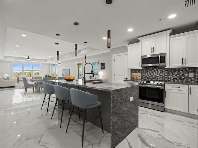 kitchen featuring decorative backsplash, visible vents, appliances with stainless steel finishes, a sink, and an island with sink
