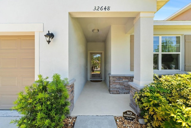property entrance with stucco siding, an attached garage, and stone siding