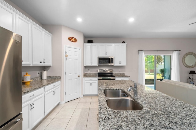 kitchen featuring appliances with stainless steel finishes, a sink, light tile patterned floors, stone counters, and white cabinetry