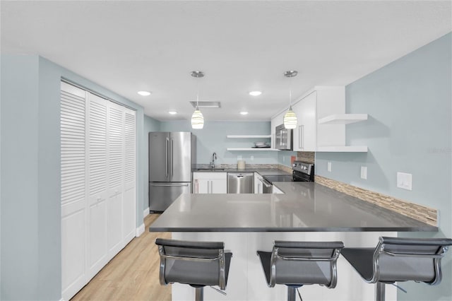 4450 Gulf Blvd Unit 114, St Pete Beach, FL 33706 - kitchen featuring appliances with stainless steel finishes, open shelves, a peninsula, light wood finished floors, and hanging light fixtures