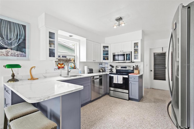 kitchen with a sink, light stone countertops, a peninsula, appliances with stainless steel finishes, and white cabinetry