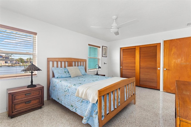 bedroom with speckled floor, ceiling fan, multiple windows, and two closets