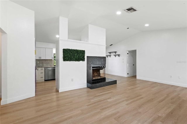 unfurnished living room with a tile fireplace, vaulted ceiling, visible vents, and light wood-style floors