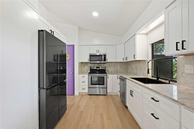 kitchen featuring vaulted ceiling, a sink, white cabinetry, backsplash, and appliances with stainless steel finishes