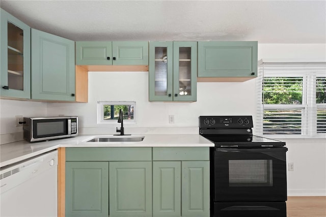 kitchen with white dishwasher, a sink, green cabinets, stainless steel microwave, and black range with electric stovetop