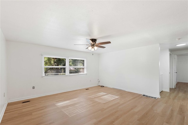 spare room featuring light wood-type flooring, visible vents, baseboards, and ceiling fan