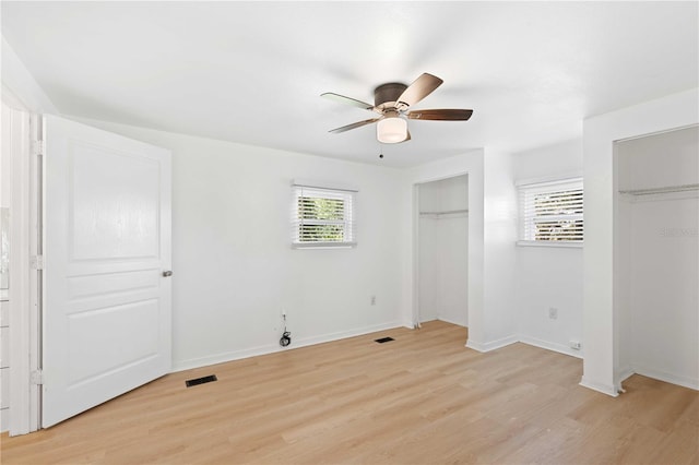 unfurnished bedroom featuring two closets, a ceiling fan, baseboards, and light wood-type flooring