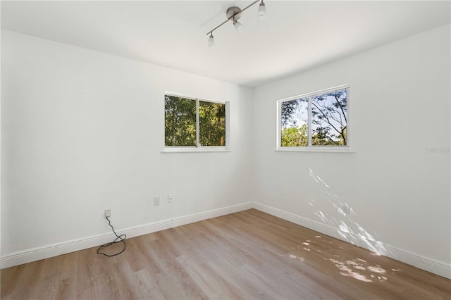 unfurnished room featuring baseboards, track lighting, and wood finished floors