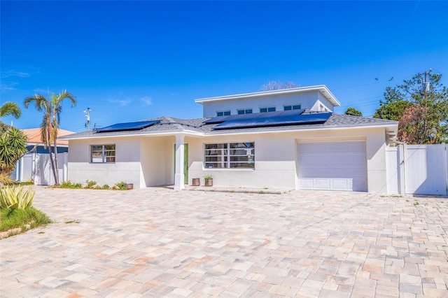 233 45th Ave, St Pete Beach, FL 33706 - view of front of home with stucco siding, a garage, roof mounted solar panels, and decorative driveway