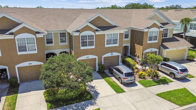 view of front of property with an attached garage, driveway, stucco siding, and roof with shingles