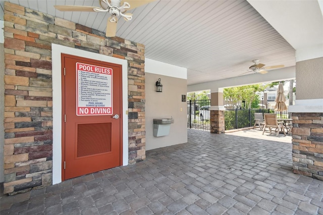 view of exterior entry with fence, stone siding, and ceiling fan