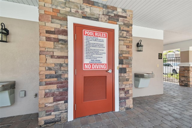 doorway to property with stone siding, stucco siding, and fence