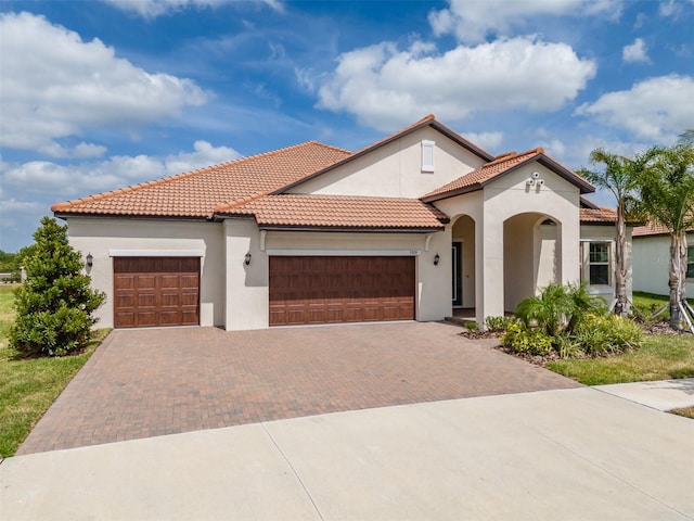 mediterranean / spanish house featuring an attached garage, a tiled roof, stucco siding, and decorative driveway