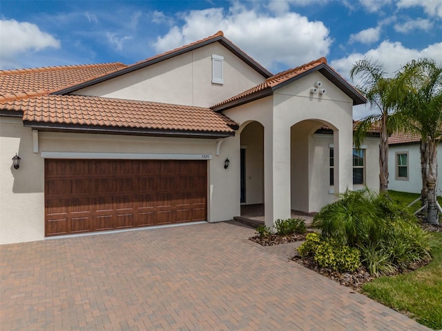 mediterranean / spanish home with stucco siding, a tile roof, decorative driveway, and a garage
