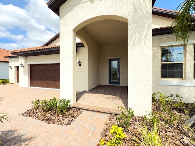 entrance to property featuring an attached garage, decorative driveway, and stucco siding