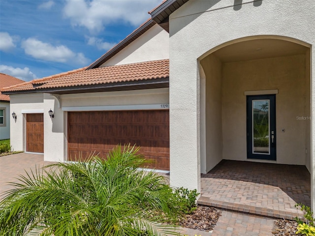 entrance to property featuring stucco siding, a tile roof, and a garage