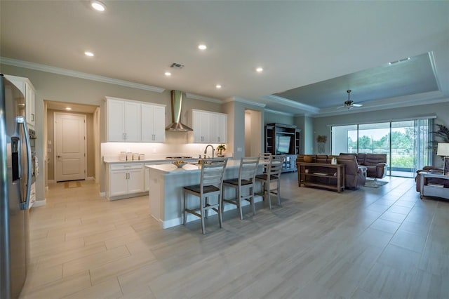 kitchen featuring crown molding, open floor plan, a breakfast bar area, wall chimney exhaust hood, and stainless steel refrigerator with ice dispenser
