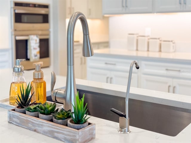 details featuring white cabinets, a sink, light stone counters, and double oven