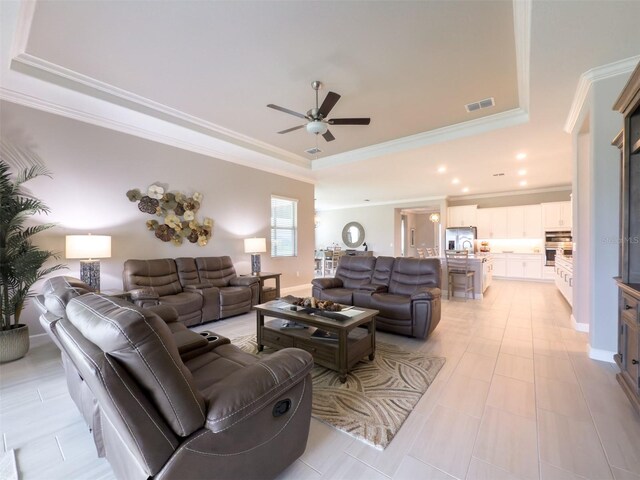 living room with recessed lighting, a tray ceiling, visible vents, a ceiling fan, and ornamental molding