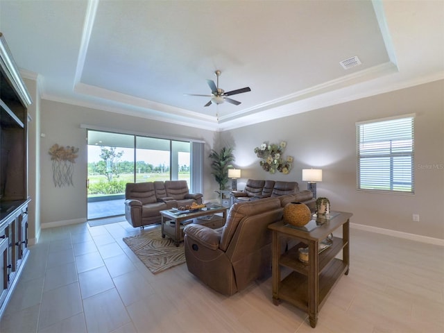 living area with a tray ceiling, crown molding, a ceiling fan, and baseboards