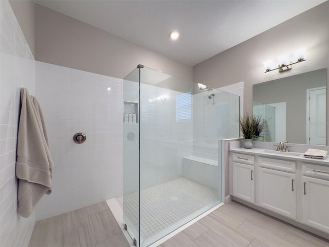 bathroom with wood finished floors, vanity, and tiled shower