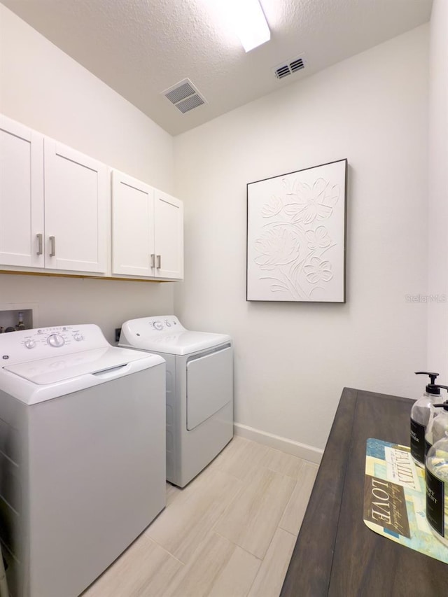 washroom featuring cabinet space, visible vents, baseboards, and separate washer and dryer