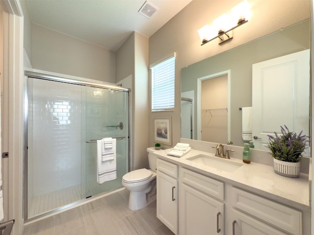 full bath with a stall shower, toilet, visible vents, vanity, and a walk in closet