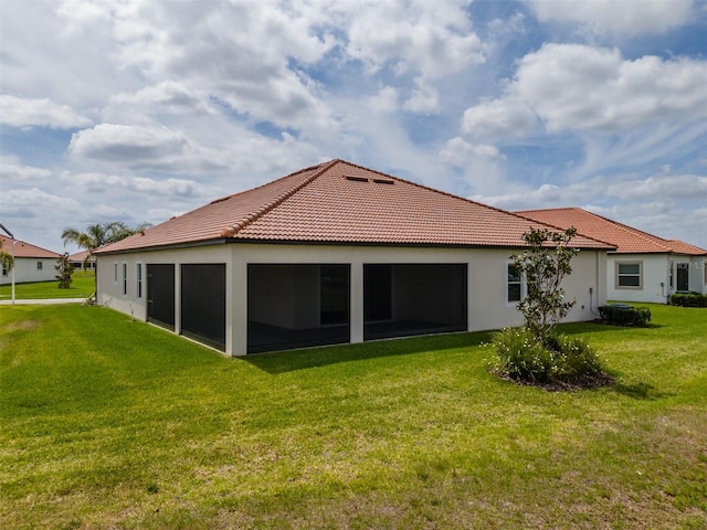 rear view of house with stucco siding, a tile roof, and a yard