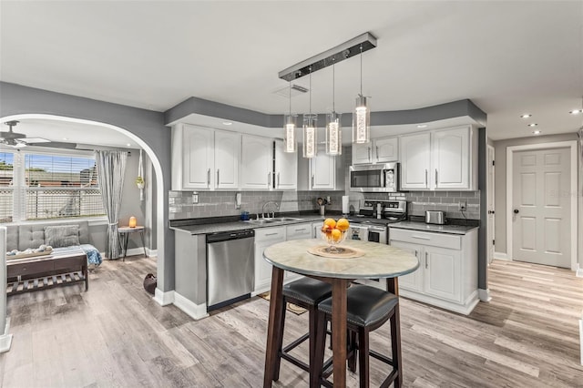 1344 Dartmouth Dr, Holiday, FL 34691 - kitchen featuring dark countertops, arched walkways, stainless steel appliances, baseboards, and white cabinetry