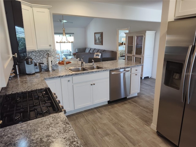 kitchen with white cabinets, a sink, light wood-style floors, a peninsula, and appliances with stainless steel finishes