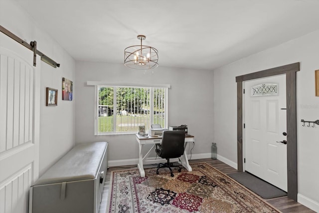 office space featuring baseboards, wood finished floors, a notable chandelier, and a barn door