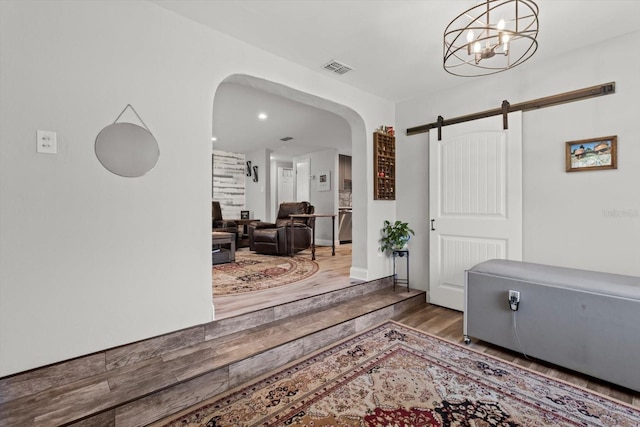 entrance foyer with a barn door, wood finished floors, a chandelier, arched walkways, and visible vents