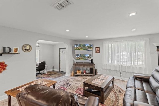 living room with arched walkways, wood finished floors, visible vents, and baseboards