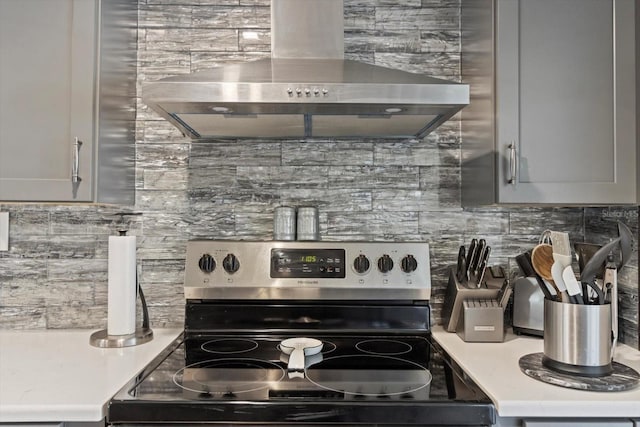 kitchen featuring wall chimney exhaust hood, tasteful backsplash, electric stove, and light countertops
