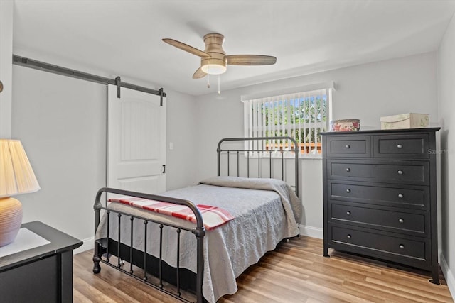bedroom featuring a barn door, a ceiling fan, and light wood-type flooring