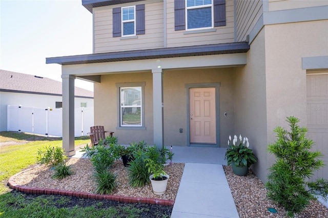 view of exterior entry featuring fence, covered porch, and stucco siding