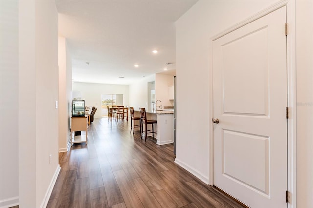 corridor featuring recessed lighting, dark wood finished floors, baseboards, and a sink